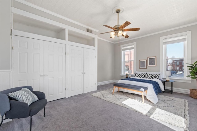 carpeted bedroom featuring visible vents, two closets, baseboards, ceiling fan, and ornamental molding