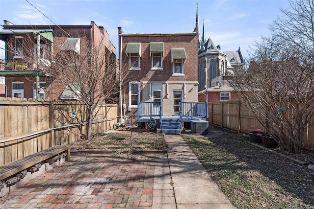 rear view of property with brick siding, central AC unit, and a fenced backyard