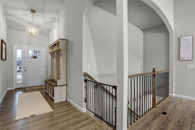 foyer entrance with arched walkways, an inviting chandelier, baseboards, and wood finished floors