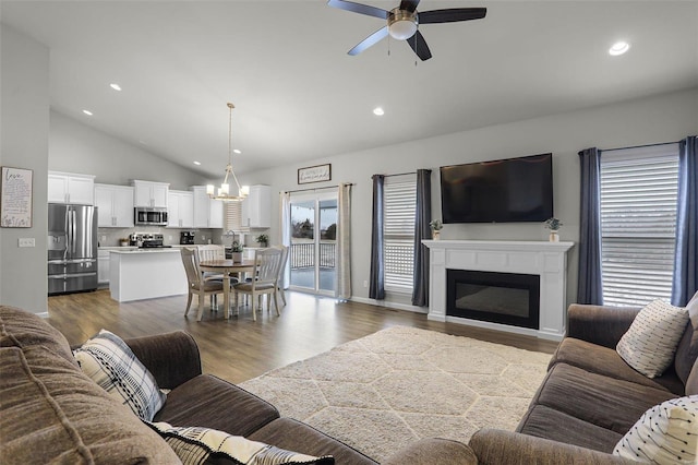 living room with high vaulted ceiling, recessed lighting, a glass covered fireplace, ceiling fan with notable chandelier, and light wood-type flooring