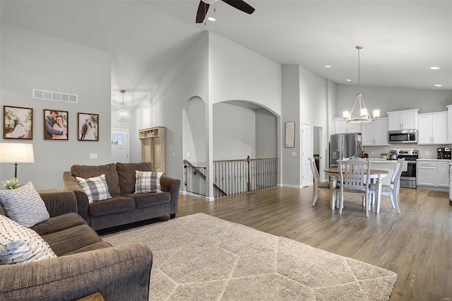 living area featuring visible vents, light wood finished floors, high vaulted ceiling, recessed lighting, and ceiling fan with notable chandelier