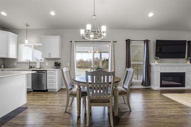 dining area featuring dark wood finished floors, a glass covered fireplace, a notable chandelier, and recessed lighting