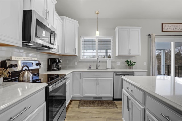 kitchen with a sink, decorative backsplash, white cabinets, appliances with stainless steel finishes, and pendant lighting