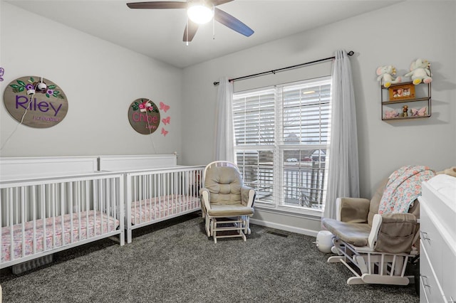 carpeted bedroom with baseboards, a crib, visible vents, and a ceiling fan