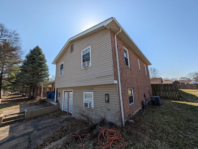 view of side of property featuring fence, brick siding, central AC, and a lawn