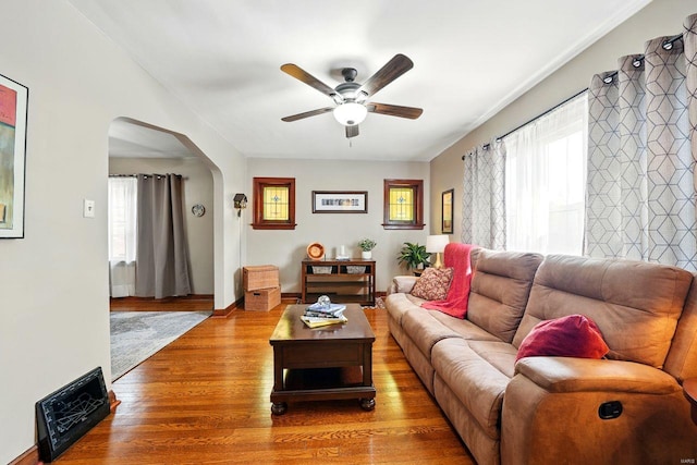 living area with wood finished floors, ceiling fan, and arched walkways
