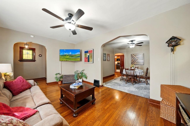 living area with hardwood / wood-style flooring, a ceiling fan, baseboards, and arched walkways