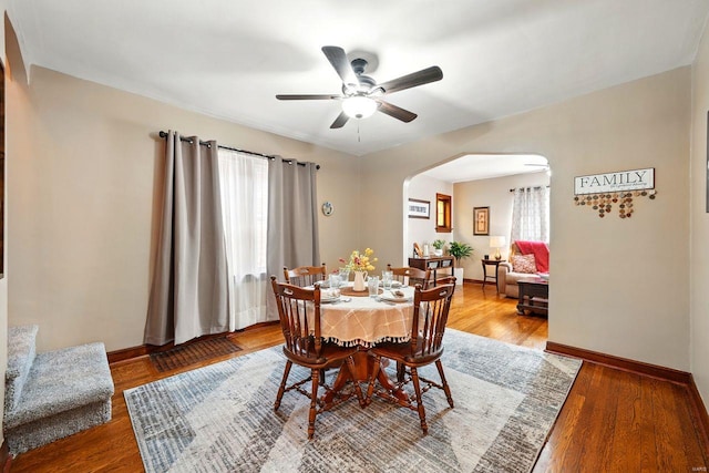 dining space with wood finished floors, a ceiling fan, baseboards, and arched walkways
