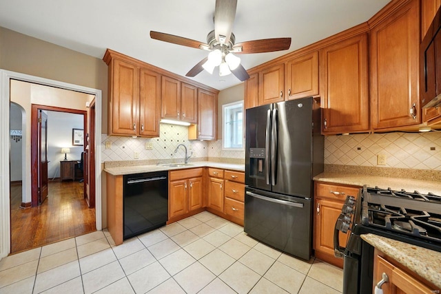 kitchen with a sink, light tile patterned floors, ceiling fan, brown cabinetry, and black appliances