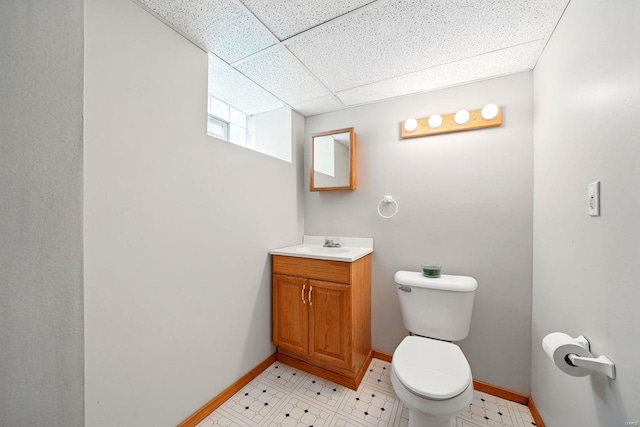 half bath featuring toilet, a drop ceiling, vanity, and baseboards