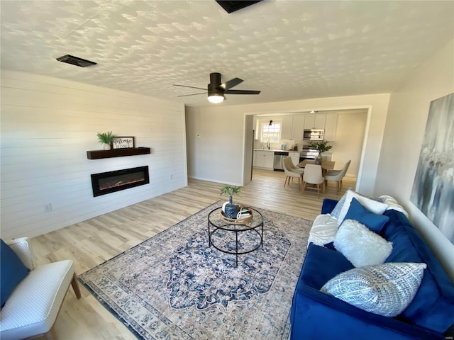 living room featuring light wood finished floors, visible vents, a textured ceiling, and a glass covered fireplace