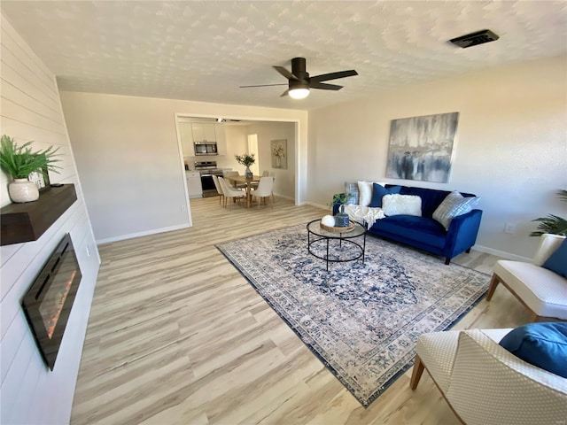 living room featuring a textured ceiling, light wood-style flooring, visible vents, and a large fireplace