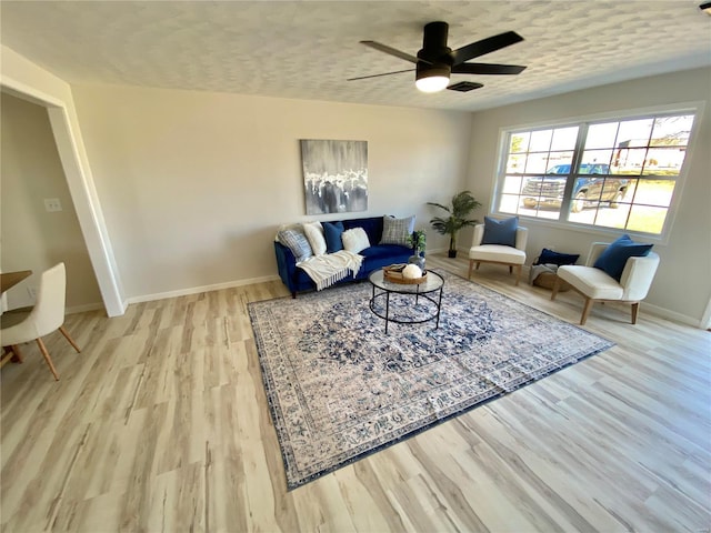 living room featuring ceiling fan, baseboards, a textured ceiling, and wood finished floors