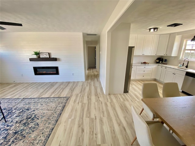 kitchen with light wood-style flooring, a sink, a glass covered fireplace, white cabinetry, and appliances with stainless steel finishes