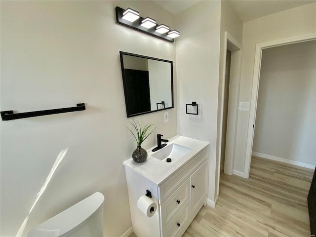 half bath with baseboards, toilet, wood finished floors, and vanity