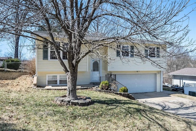 split foyer home featuring a garage, concrete driveway, a front yard, and fence