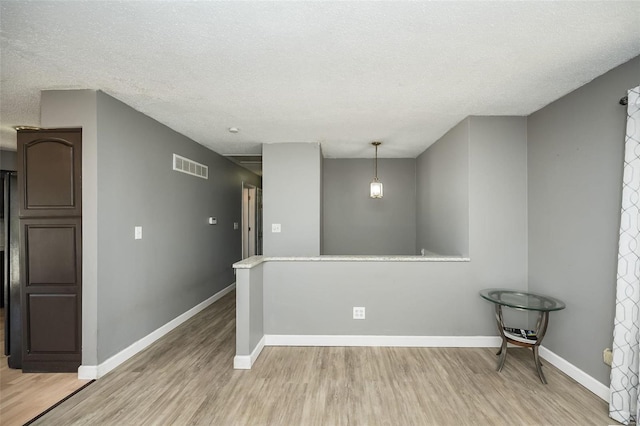 spare room with a textured ceiling, light wood-style floors, visible vents, and baseboards