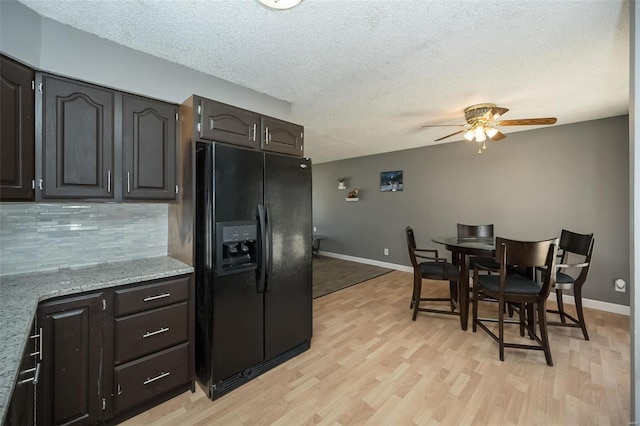 kitchen featuring light wood finished floors, black fridge with ice dispenser, a textured ceiling, and decorative backsplash