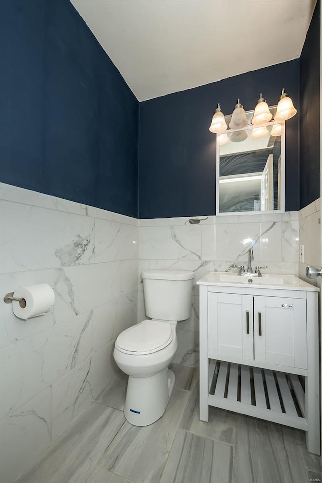 bathroom with toilet, tile walls, wainscoting, and vanity