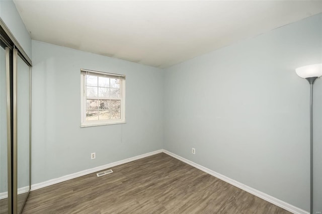 unfurnished bedroom featuring wood finished floors, visible vents, a closet, and baseboards