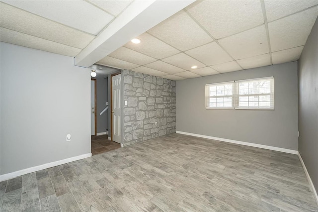 basement with a drop ceiling, baseboards, and wood finished floors