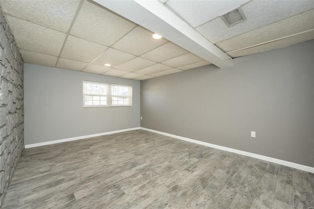 spare room with wood finished floors, visible vents, a drop ceiling, and baseboards