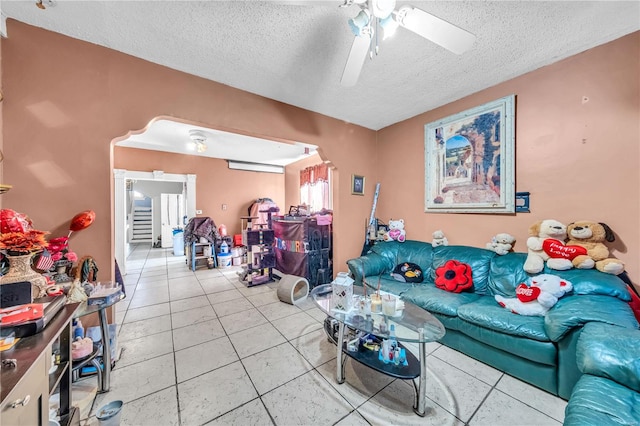 living room featuring light tile patterned floors, arched walkways, a textured ceiling, and a ceiling fan