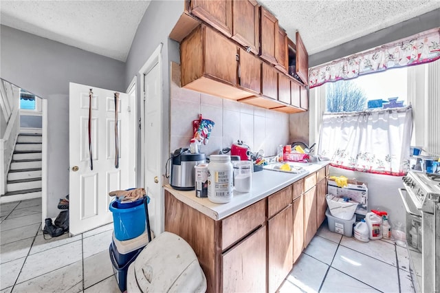 kitchen featuring stainless steel gas stove, backsplash, a textured ceiling, brown cabinetry, and light countertops