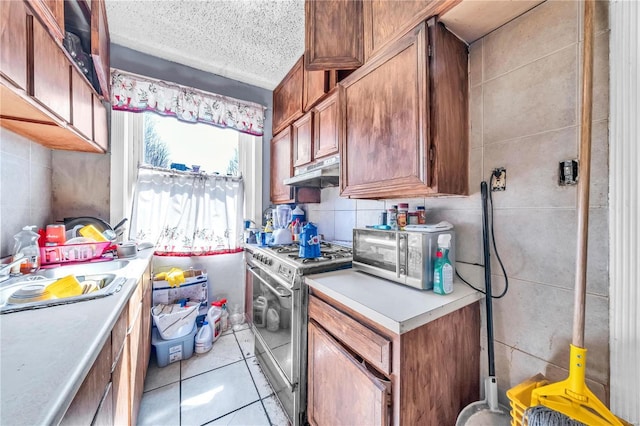 kitchen with under cabinet range hood, backsplash, appliances with stainless steel finishes, and light countertops