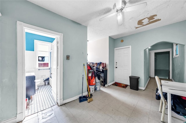 interior space with baseboards, a ceiling fan, arched walkways, and a textured ceiling