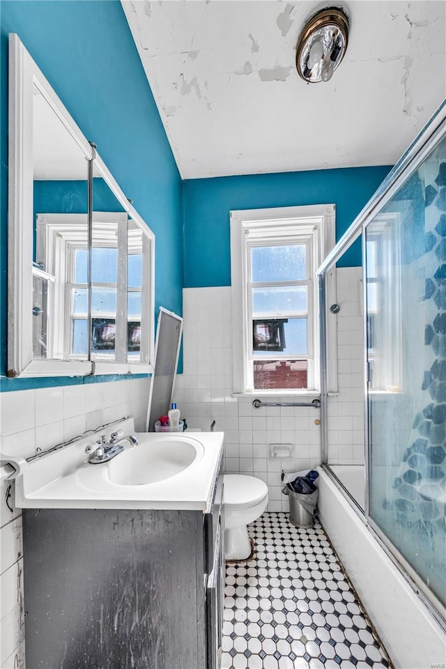 full bath featuring bath / shower combo with glass door, toilet, tile walls, and vanity