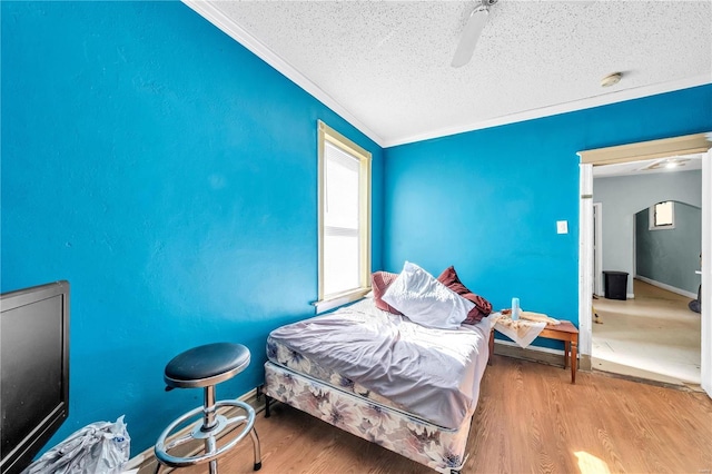 bedroom with a ceiling fan, ornamental molding, wood finished floors, and a textured ceiling