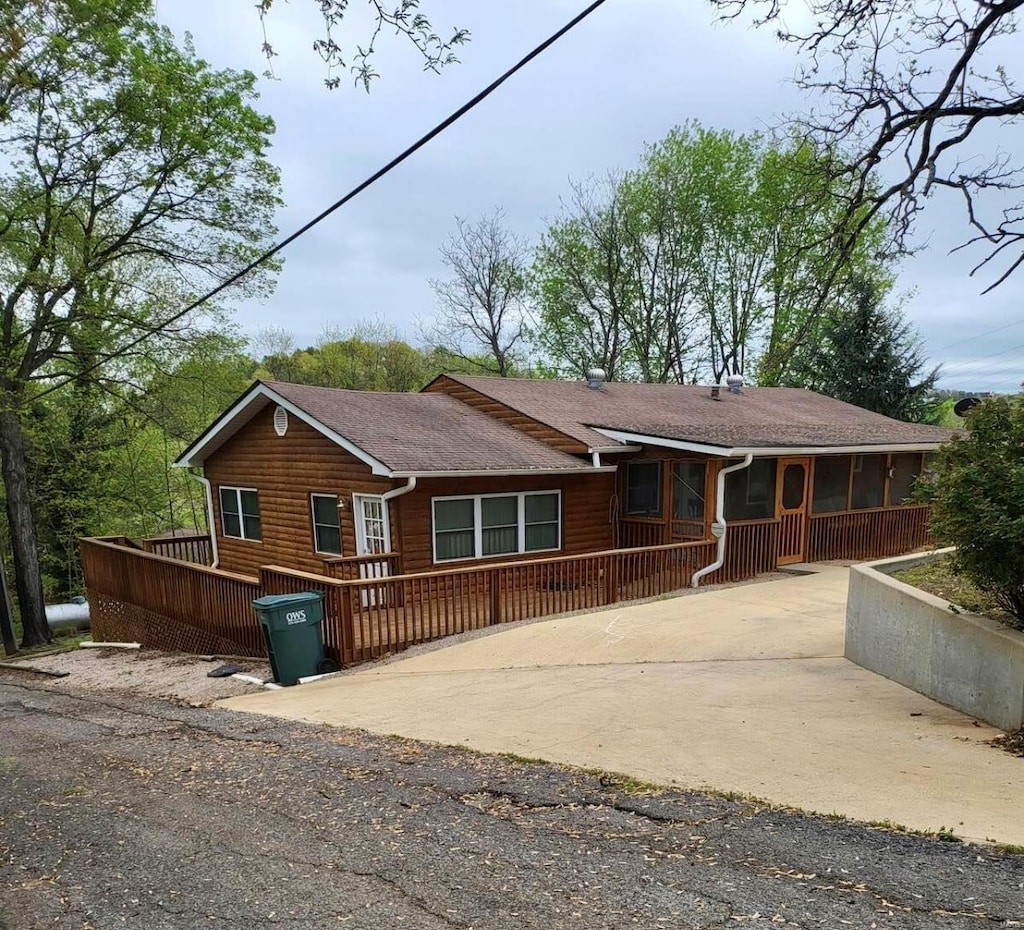 view of front of property featuring concrete driveway, a wooden deck, and log veneer siding