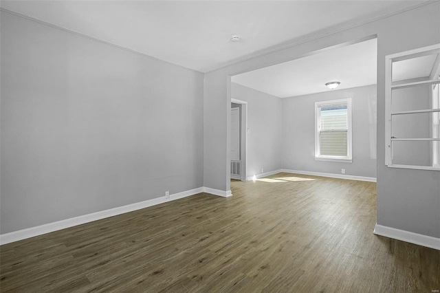 spare room with dark wood-style floors, visible vents, and baseboards
