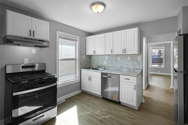 kitchen featuring a sink, decorative backsplash, stainless steel appliances, white cabinets, and under cabinet range hood