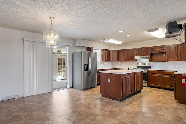 kitchen with under cabinet range hood, a center island with sink, light countertops, stainless steel appliances, and a textured ceiling