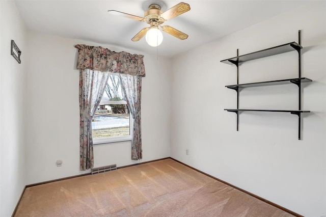 carpeted spare room with visible vents, baseboards, and a ceiling fan