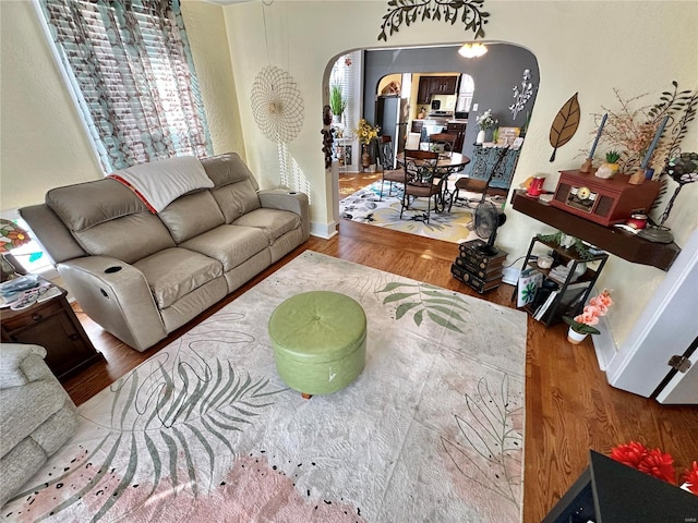 living room with arched walkways, baseboards, and wood finished floors