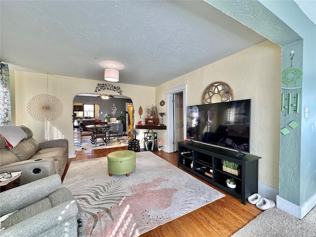 living room with a textured ceiling, wood finished floors, arched walkways, baseboards, and a textured wall