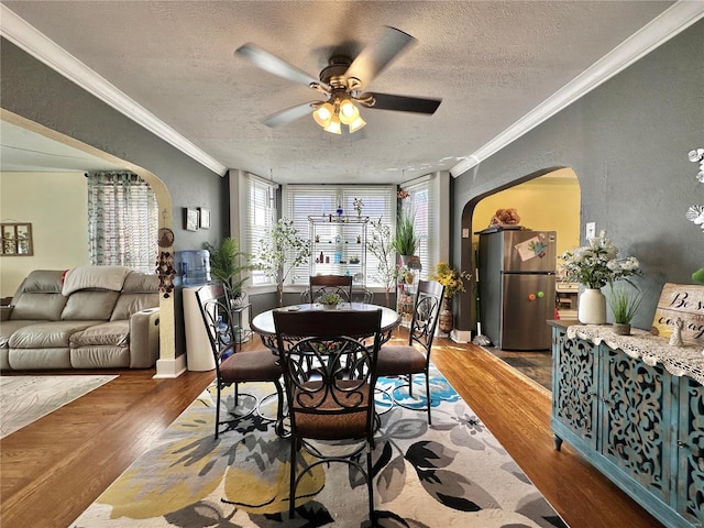 dining area with crown molding, wood finished floors, and arched walkways