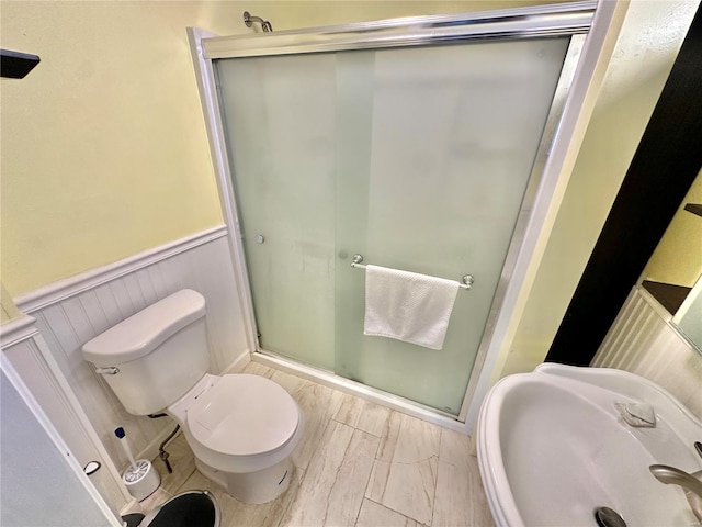 full bath with a stall shower, toilet, a wainscoted wall, and a sink