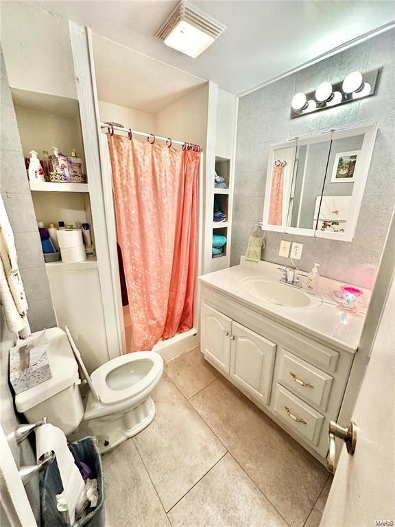 bathroom with toilet, a stall shower, tile walls, tile patterned flooring, and vanity