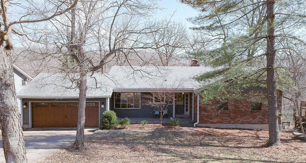 view of front of house featuring brick siding, a shingled roof, a chimney, driveway, and an attached garage