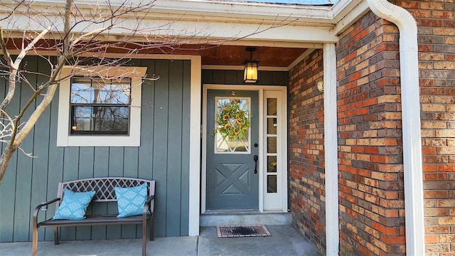 doorway to property featuring brick siding, covered porch, and board and batten siding