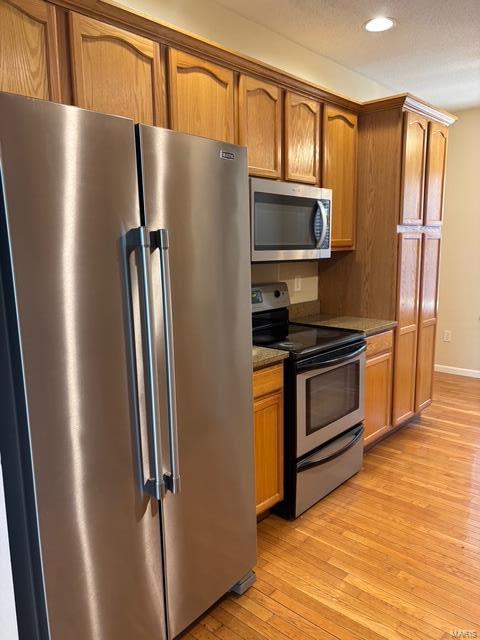 kitchen featuring recessed lighting, appliances with stainless steel finishes, brown cabinetry, and light wood finished floors