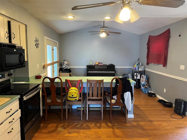 kitchen with baseboards, black microwave, stainless steel electric stove, vaulted ceiling, and wood finished floors