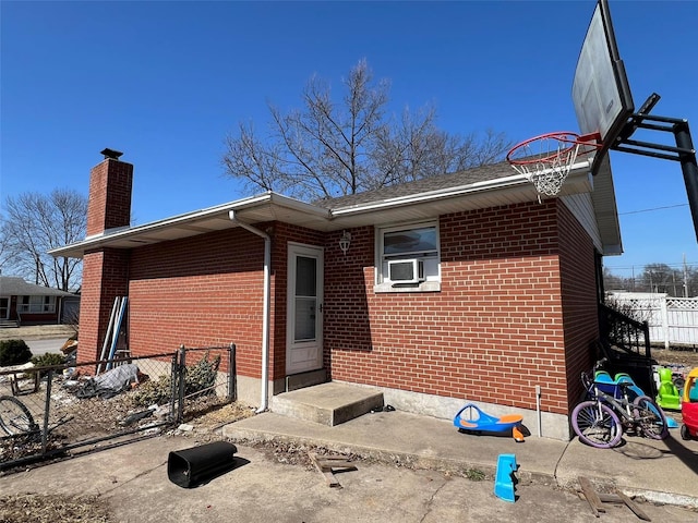 rear view of house featuring brick siding, a chimney, and fence