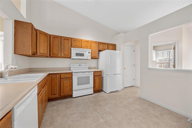 kitchen featuring white appliances, baseboards, a sink, light countertops, and brown cabinets