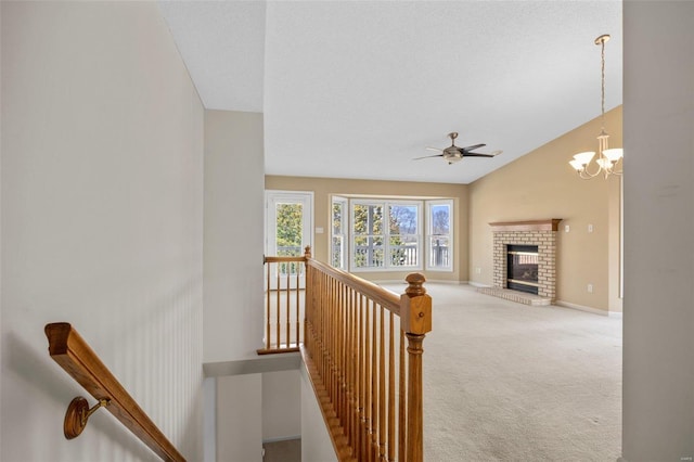 stairway with lofted ceiling, ceiling fan with notable chandelier, carpet flooring, baseboards, and a brick fireplace