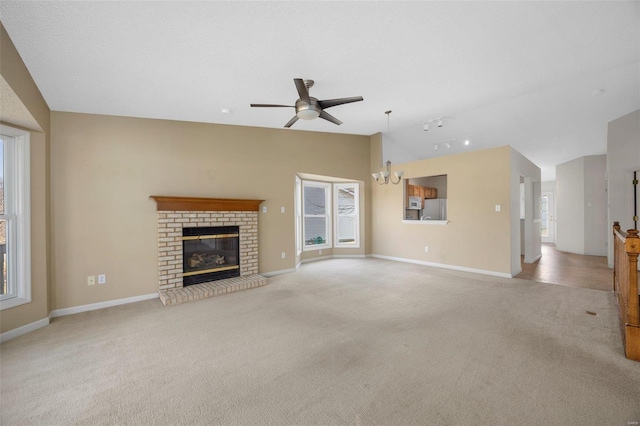 unfurnished living room with lofted ceiling, a healthy amount of sunlight, ceiling fan with notable chandelier, and light carpet